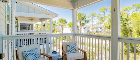 A covered porch with wooden furniture, a ceiling fan, and a view of the surrounding neighborhood.