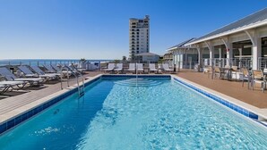 Una piscina con sillones de descanso y un edificio al fondo.