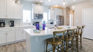 Una cocina moderna con armarios blancos, una isla central y sillas de madera.