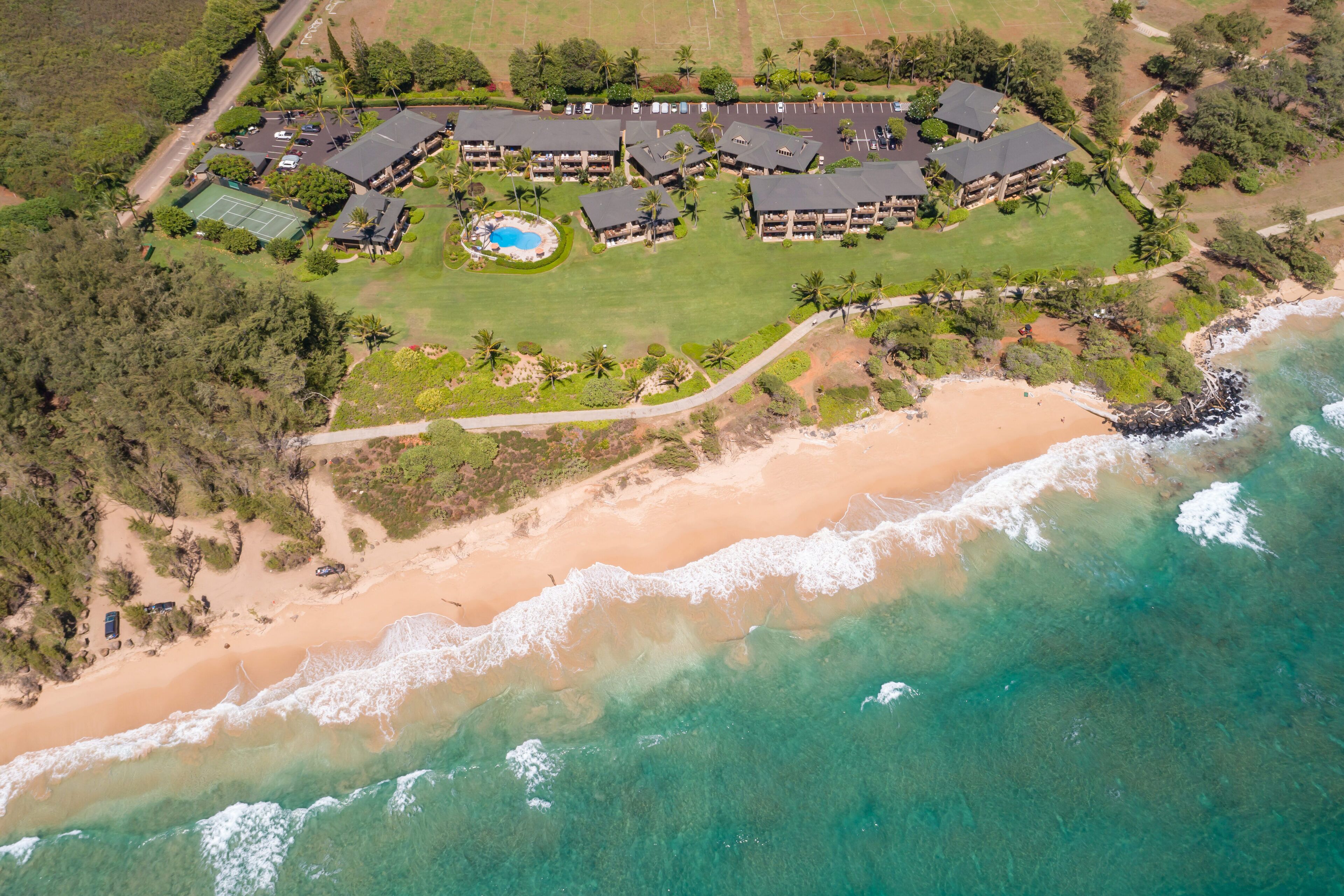 Eine Luftaufnahme eines Resorts mit mehreren Gebäuden, einem Strand und einem Schwimmbad.