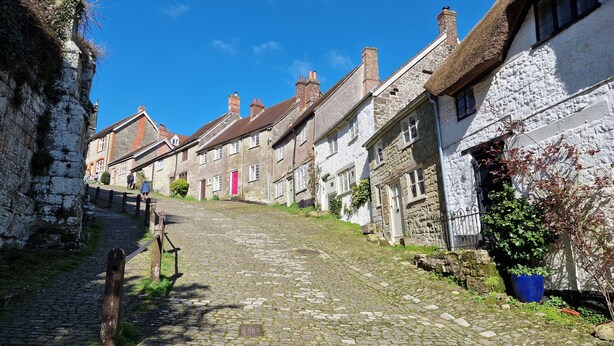 Una calle adoquinada flanqueada por edificios de piedra tradicionales, algunos con techos de paja.