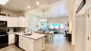 A modern kitchen with white cabinets, a central island, and a dining area with a sofa and chairs.