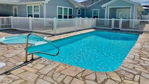 A swimming pool with a stone deck, a white fence, and a small dock.