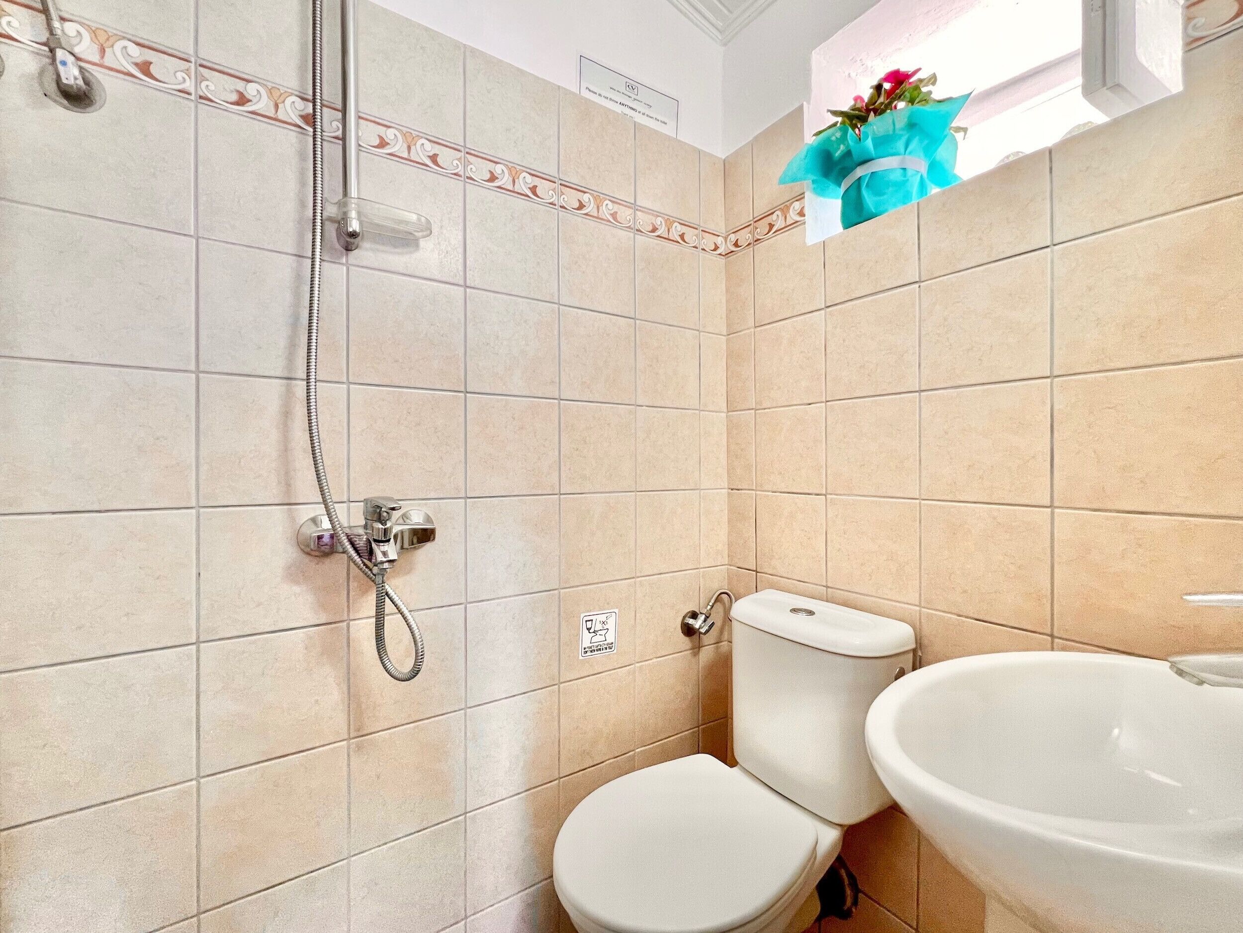 Ein Badezimmer mit beigen Fliesen, einer Dusche, einer Toilette und einem Waschbecken.