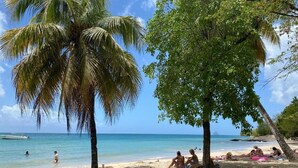 A beach with palm trees, people relaxing, and a boat in the water. - Studio Ti Paradise Magnifique vue mer et Diamant (Sainte-Luce)