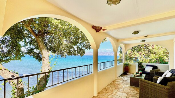 Un balcone con pavimento in pietra, un divano in vimini e vista sul mare.