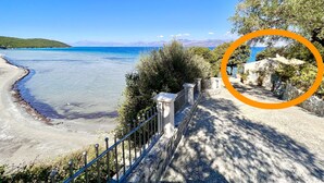 Un sentiero costiero con un muro in pietra e una ringhiera metallica, che conduce a un piccolo edificio con tetto in pietra.