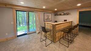 Ett rum med ett träpanelat tak, en bardisk med barstolar, en dörr som leder ut till en balkong och en inramad tavla på väggen.