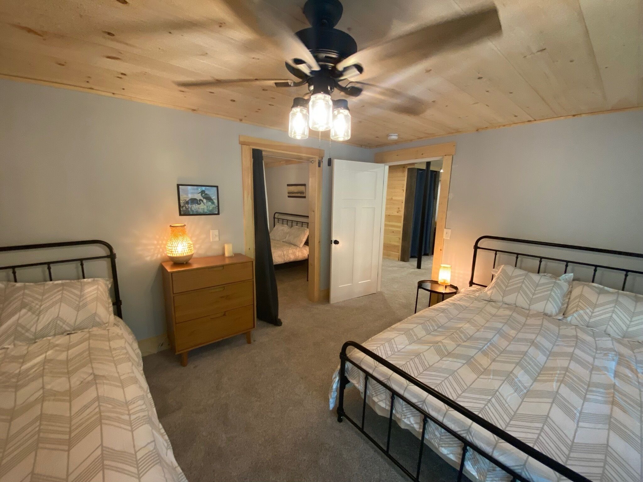 A bedroom with two beds, a wooden dresser, a ceiling fan, and a door leading to another room.