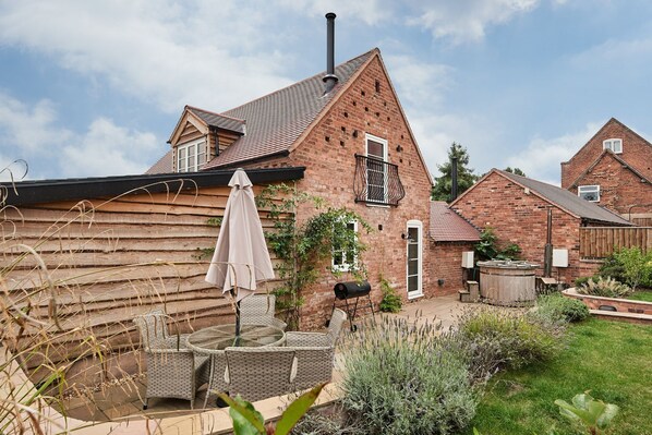 A brick house with a sloped roof, a chimney, and a garden with outdoor furniture. - Hay Bale Cottage - Luxury Cottages (Worcester)