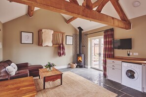 A cozy living room with a fireplace, a sofa, a coffee table, and a washing machine in the corner. - Stable Cottage - Luxury Cottages (Worcester)
