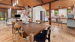 A spacious kitchen with a wooden ceiling, a dining area with a wooden table and chairs, and a large window providing a view of the outdoors.