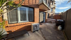 A residential backyard with a brick house, a patio with a table and chairs, a large air conditioning unit, and a water heater. - THE TERRACES UNIT 4- beautifully renovated ground floor unit. (South West Rocks)