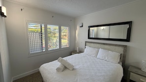 A bedroom with a bed, a nightstand, a mirror, and a window with blinds. - THE TERRACES UNIT 4- beautifully renovated ground floor unit. (South West Rocks)