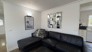 Een moderne woonkamer met een zwarte leren bank, een kussen met zebraprint, een ingelijst foto van een strand en een reflecterend kunstwerk aan de muur.