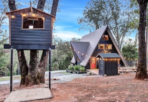 A modern cabin with a large window and a treehouse attached to a tree.