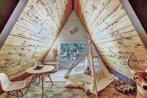 A cozy interior with a wooden tent structure, a round table, white chairs, a plush rug, and a toy train.