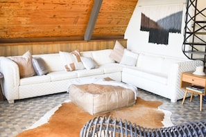 A cozy living room with a white sectional sofa, a small ottoman, a patterned rug, a cowhide rug, and a metal chair.