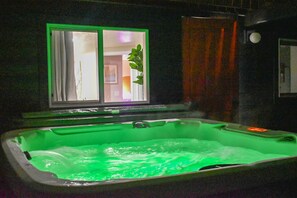 Un bain à remous à l’intérieur verdâtre, une fenêtre avec des rideaux et une plante visible à travers la fenêtre.