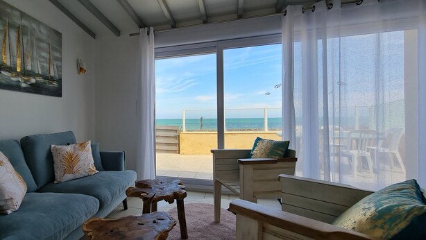 Sala de estar con sofá, una mesa de centro y vista a la playa a través de amplios ventanales.