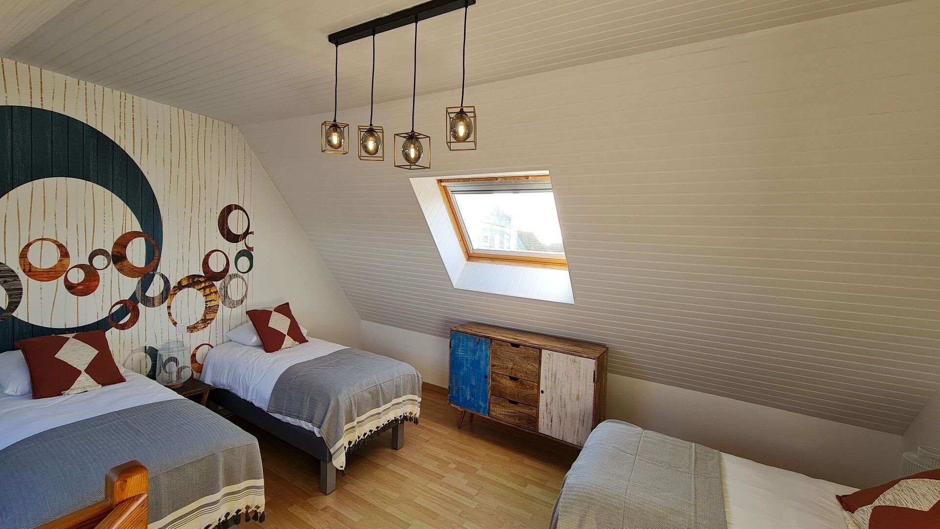 A cozy attic bedroom with two beds, a skylight, and a unique wall decor.
