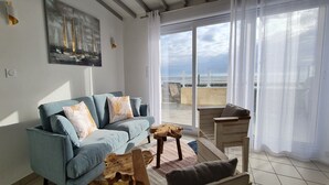 Una sala de estar con un sofá azul, una mesa de centro de madera y vista al mar a través de un ventanal.
