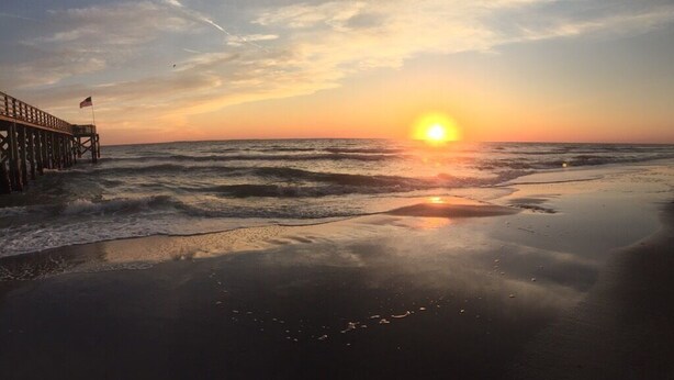 Ein Strandbild mit einem Steg, der bei Sonnenuntergang ins Meer hinausführt.