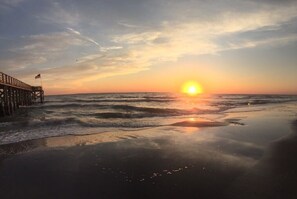 En strandscene med en moler, der strækker sig ud i havet i solnedgang.