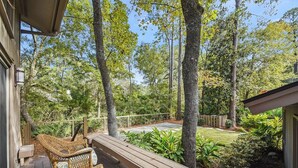 A wooden deck with wicker furniture, surrounded by trees and a well-maintained garden.