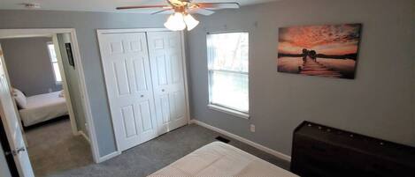 A bedroom with a bed, a ceiling fan, a window, and a door.