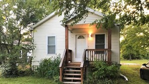A small, single-story house with a front porch and a staircase leading to the door.