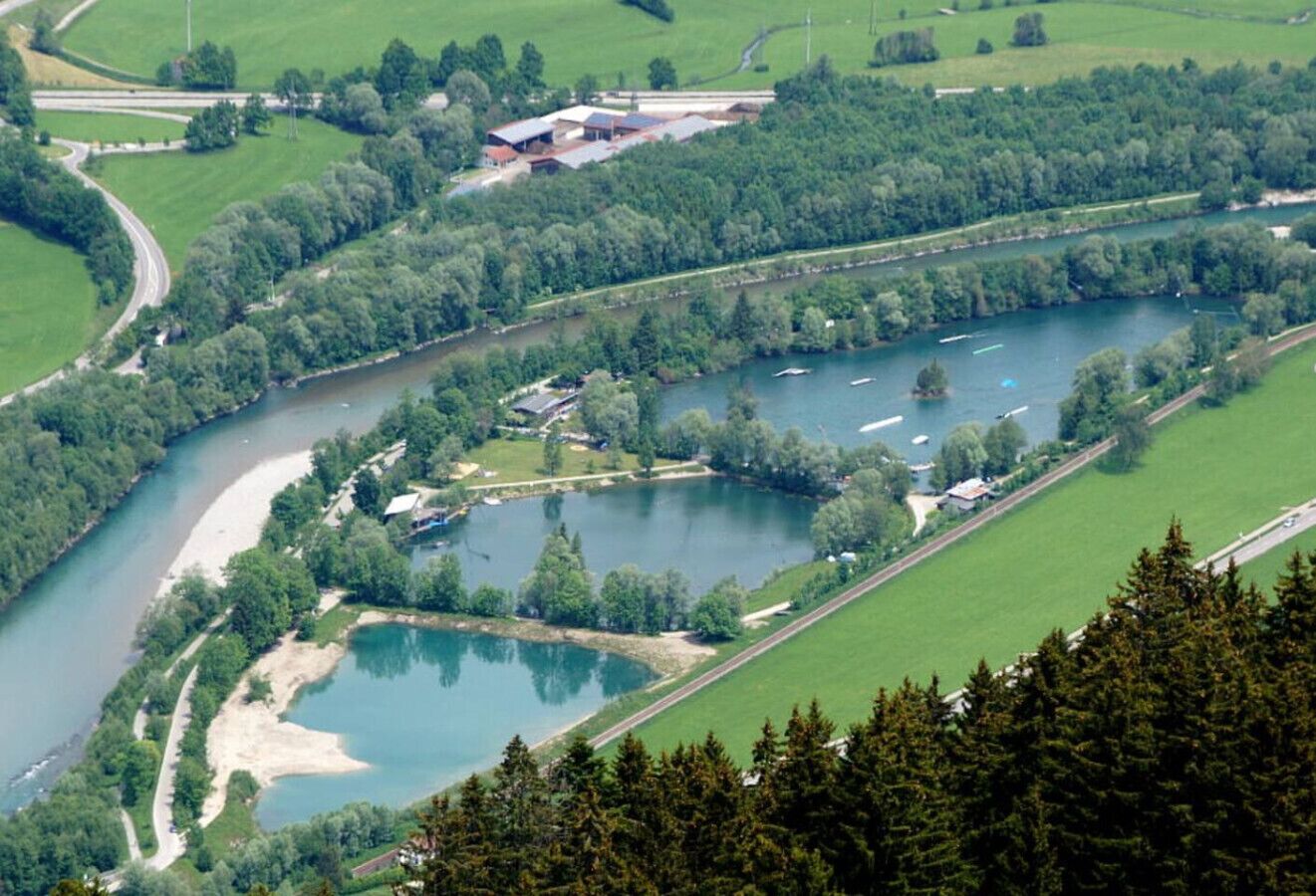 An aerial view of a riverside area with a small lake, a bridge, and a building complex.