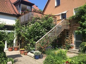 A residential building with a wooden staircase leading to a balcony, surrounded by various potted plants and flowers. - 85 m² Loft Apartment with Panoramic Views in Coburg (Coburg)