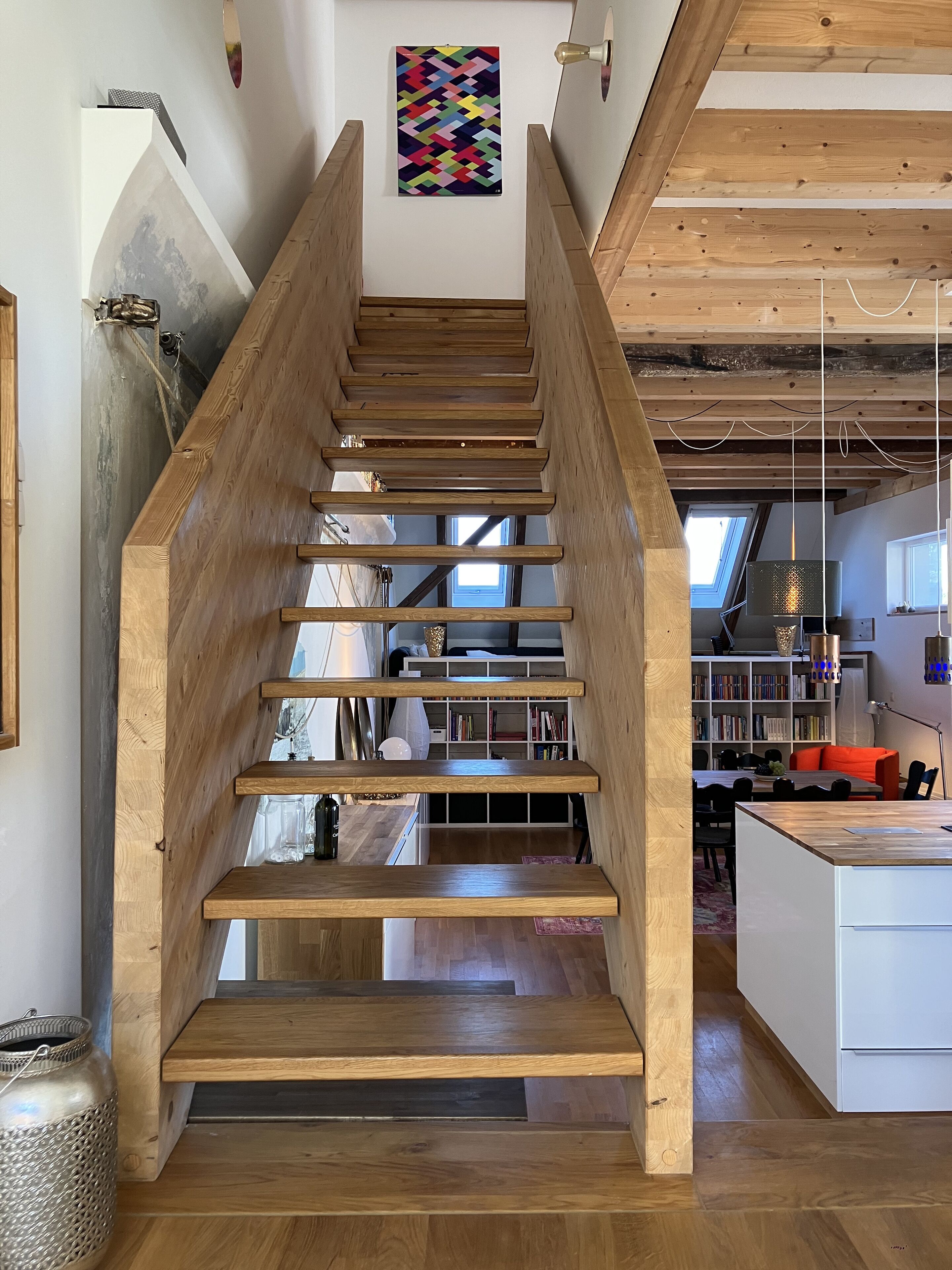 Eine Holztreppe führt zu einer Erkerzone mit Oberlichter, Bücherregalen und einem Essbereich.