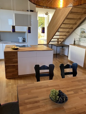 A modern kitchen with a wooden island, white cabinets, and a dining area with a wooden table and chairs. - 85 m² Loft Apartment with Panoramic Views in Coburg (Coburg)