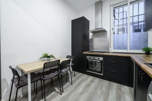 Cocina compacta con una mesa de madera, sillas negras, estufa y una ventana con vidrio esmerilado.