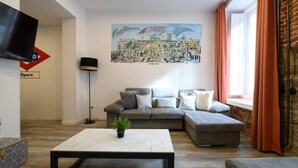 Un salón moderno con un sofá seccional gris, una mesa de centro blanca y una pintura de un paisaje urbano en la pared.