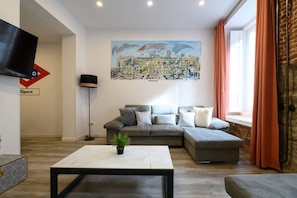 Een moderne woonkamer met een grijze hoekbank, een witte salontafel en een stadslandschap schilderij aan de muur.