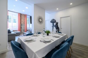 Un comedor con una mesa blanca dispuesta para cuatro personas, sillas azules y un espejo decorativo en la pared.