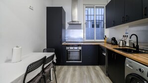 Una cocina compacta con horno integrado, lavavajillas y ventana con vistas a un paisaje urbano.