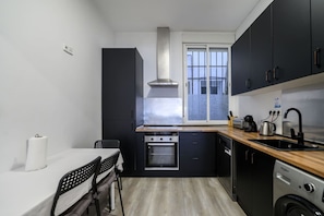 Een compacte keuken met een ingebouwde oven, een vaatwasser en een raam met uitzicht op een stadsgezicht.