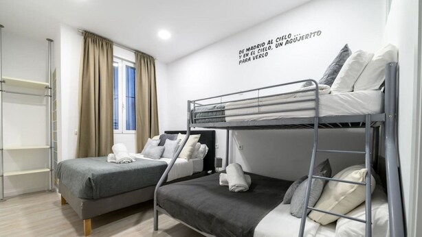 Una habitación de hotel moderna con literas, una ventana con cortinas, un estante en la pared y una lámpara en el techo.