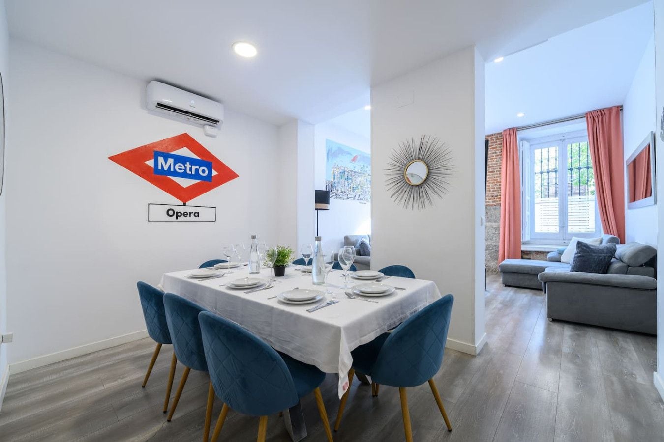 Un coin repas avec une table dressée pour six personnes, des chaises bleues et un panneau du métro accroché au mur.