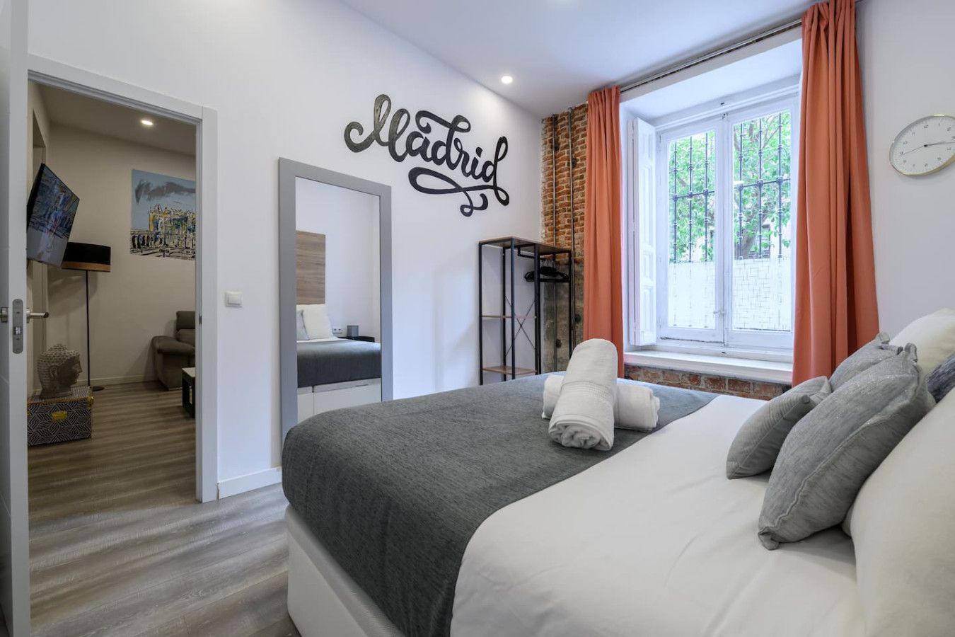 A modern bedroom with a bed, a mirror, a window with curtains, and a wall with the word "Madrid" written on it.
