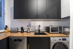 Cocina compacta con armarios oscuros, un lavamanos, un tostador, un hervidor, un microondas y una lavadora.