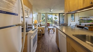 A compact kitchen with wooden cabinets, a refrigerator, a stove, and a dining area with a table and chairs. - Maui Sunset Vacation Rentals A316 (Kihei)