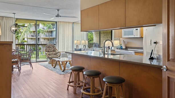 A modern kitchen with a large island, bar stools, and a view of a balcony with outdoor furniture. - Maui Sunset Vacation Rentals B206 (Kihei)