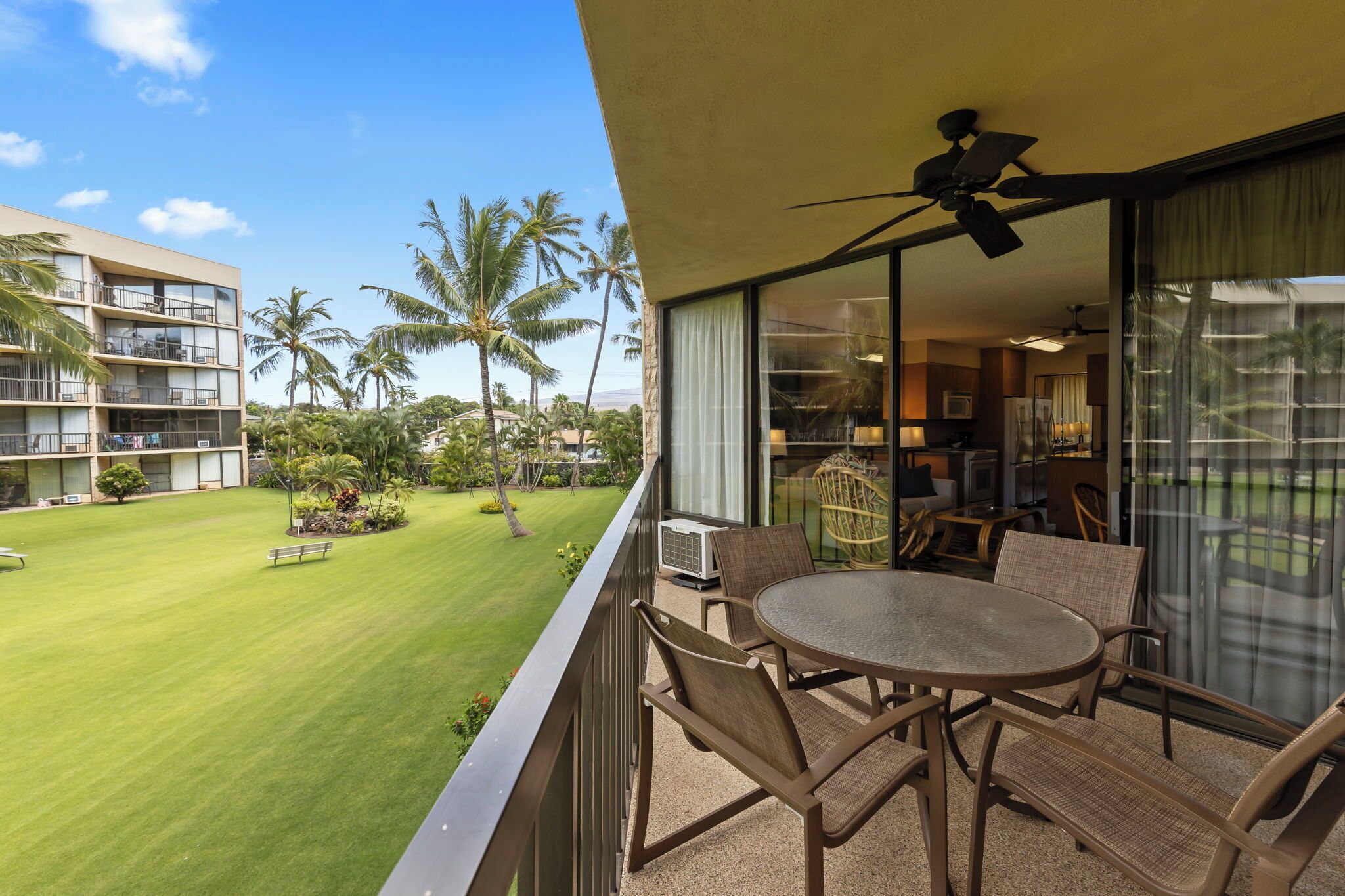 A balcony with a table and chairs, overlooking a well-maintained lawn and palm trees.
