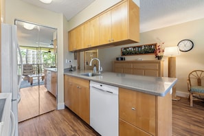 A modern kitchen with wooden cabinets, a dishwasher, a sink, and a dining area with a view of the outdoors.