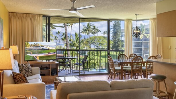 A hotel room with a balcony, a TV, a sofa, a dining table with chairs, and a ceiling fan. - Maui Sunset Vacation Rentals- B318 (Kihei)